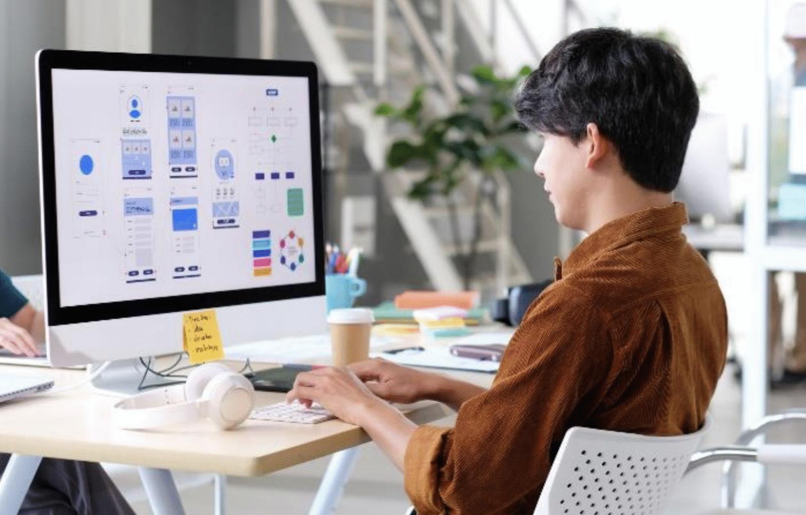Web designer fiche métier - Un web designer est sur son ordinateur en train de vérifier les maquettes de plusieurs interfaces d'application